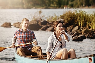 Two people in a boat on a calm lake, rowing in unison as the sun sets.